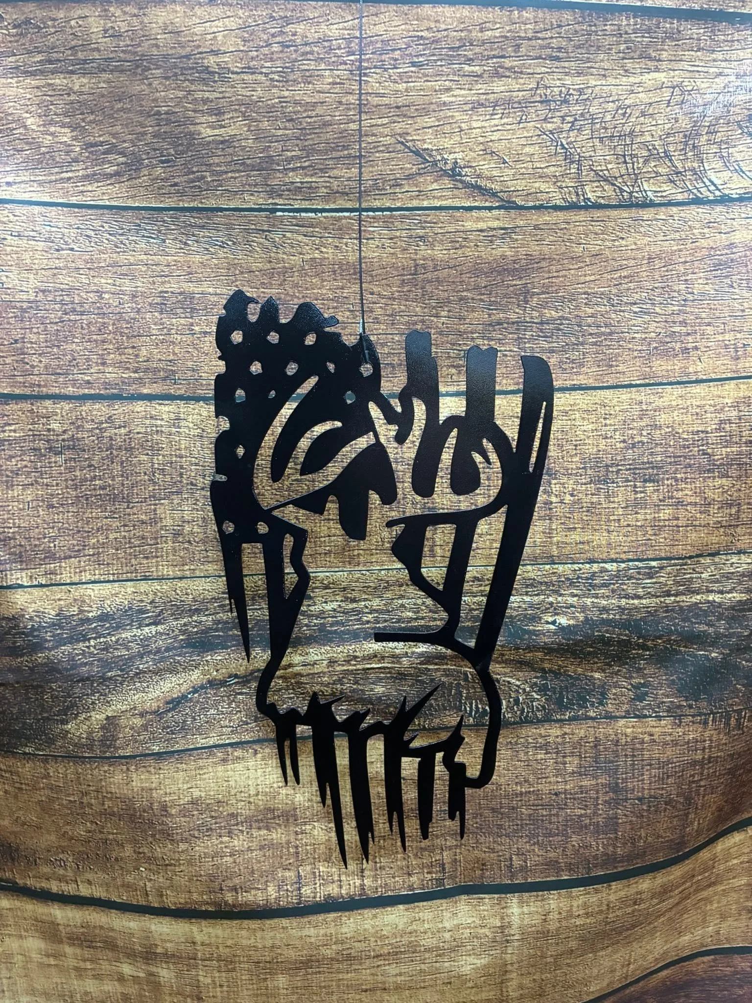 A black, cut-out metal wall art of a rooster and the word 'FARM' on a wooden surface background.