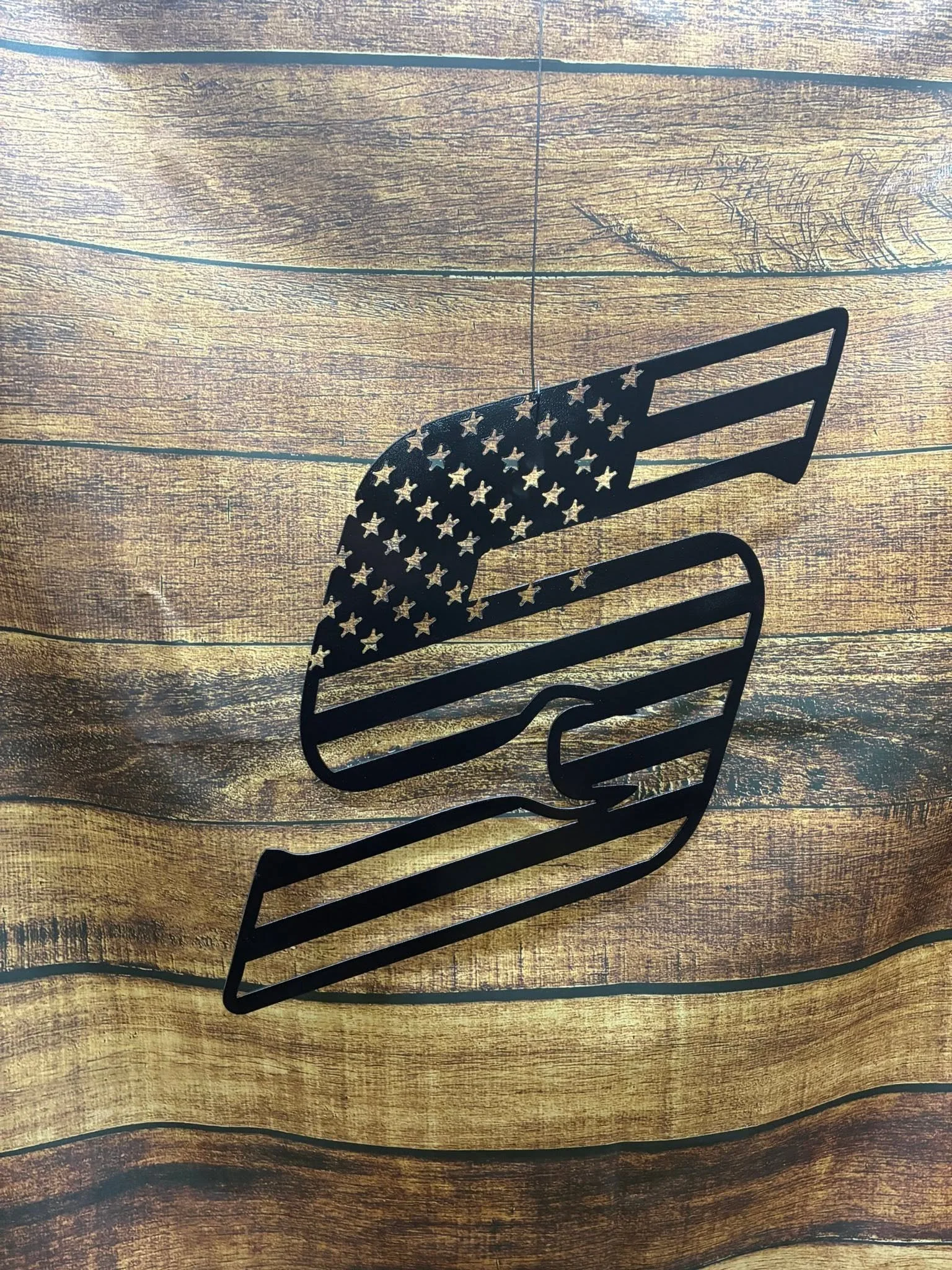 A black metal cutout of a hand holding an American flag, placed on a wooden surface.