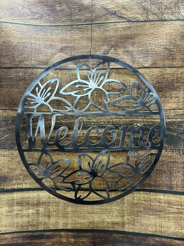 Decorative metal sign with the word 'Welcome' surrounded by butterfly motifs, placed on a wooden surface.