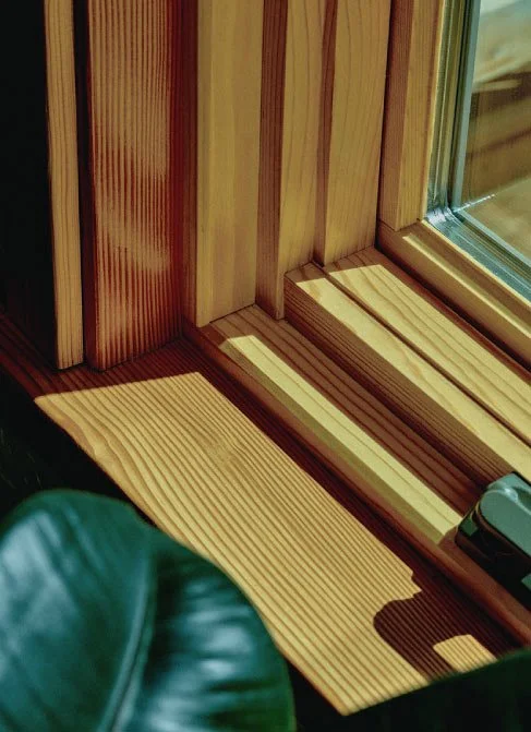 Close-up of a wooden window ledge casting shadow near a window, with part of a green leather chair visible at the bottom.