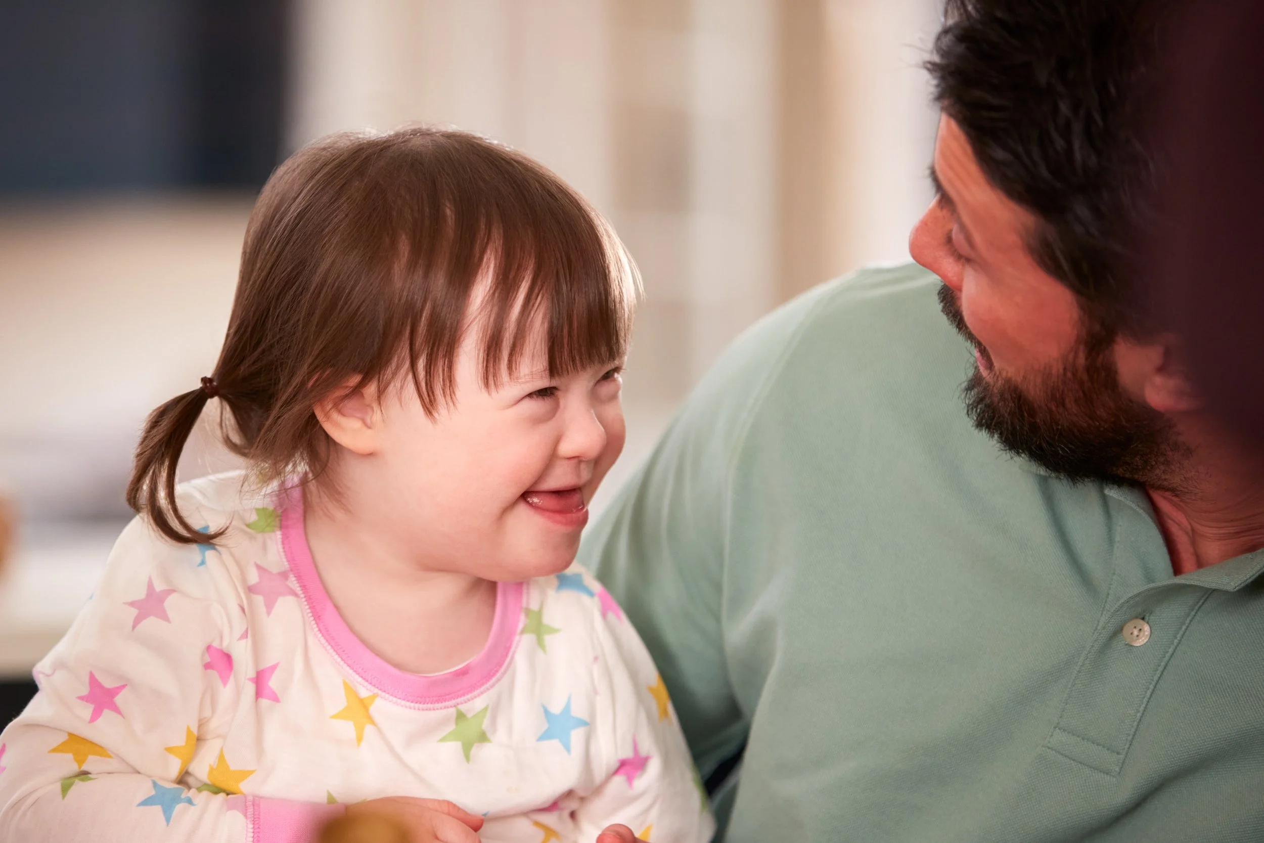 A young girl and a man sharing a joyful moment, smiling at each other in an indoor setting.