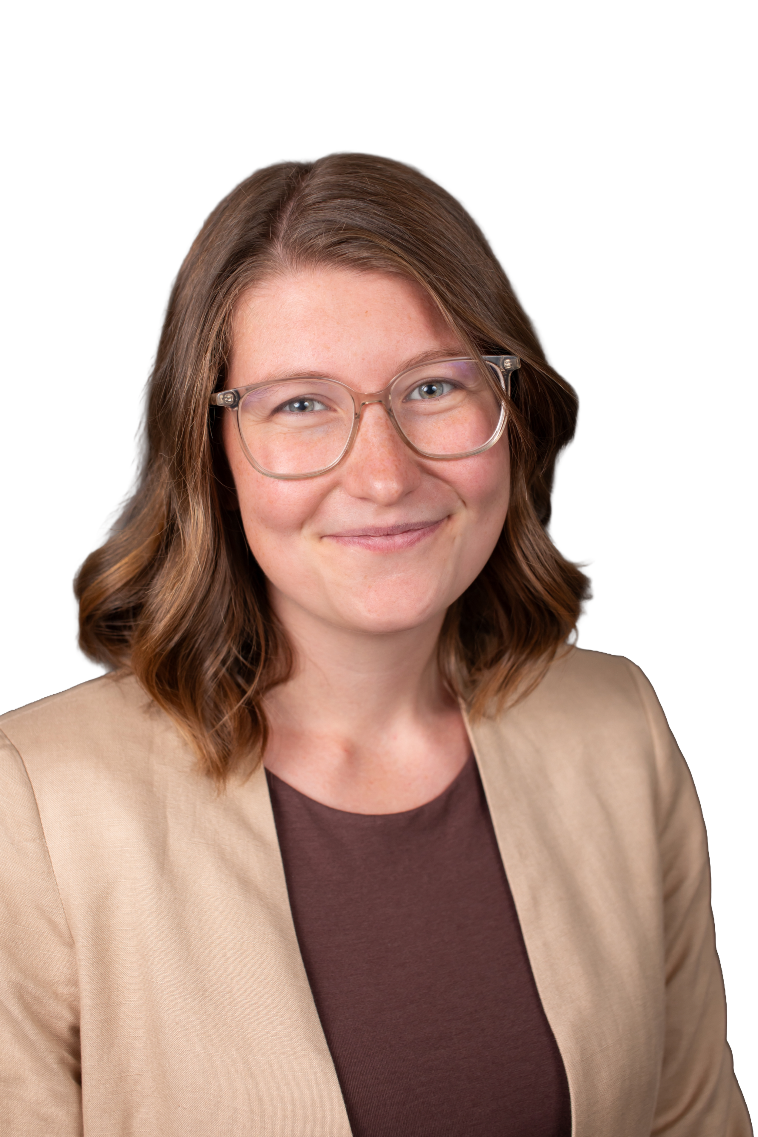 A woman with shoulder-length wavy brown hair, clear glasses, and a smile wearing a beige blazer over a dark brown top against a black background.