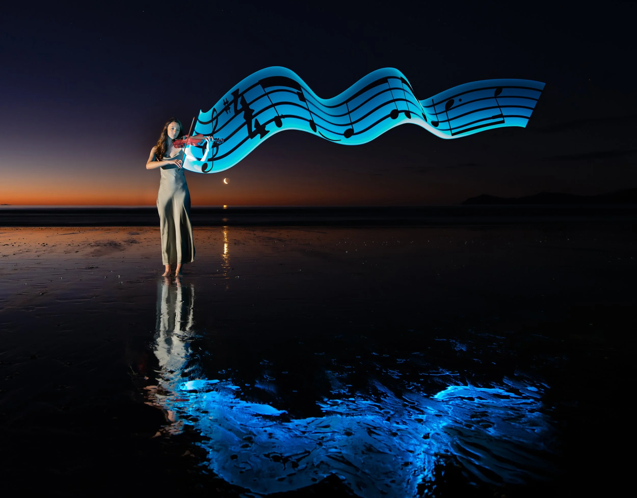 A woman plays a violin on the beach at sunset with a large, glowing musical staff floating above her, emitting blue light, and reflections can be seen on the wet sand.