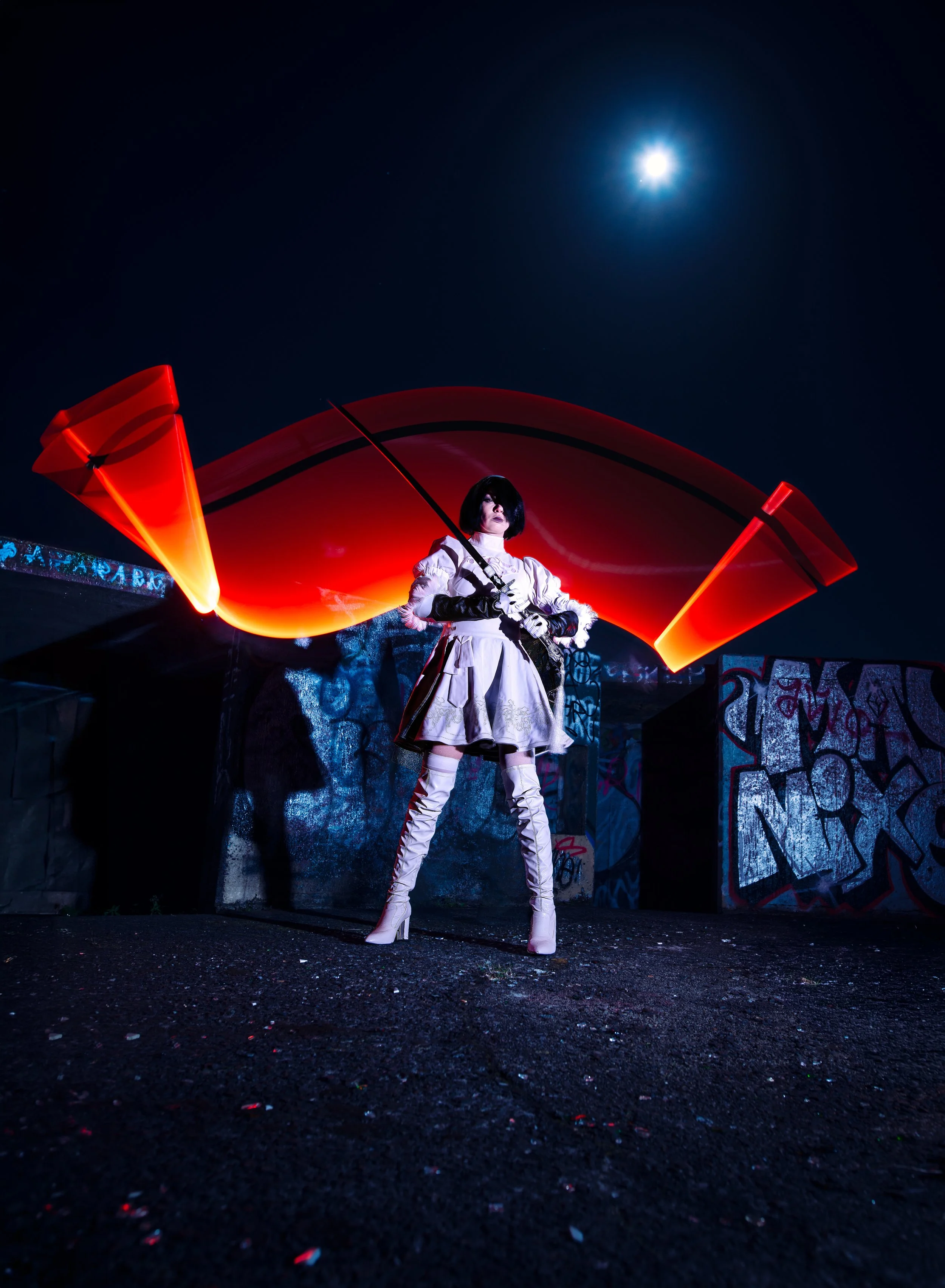 A woman dressed in a white outfit with thigh-high white boots and black gloves, standing under a bright full moon at night, holding a red umbrella with a glowing red light, in front of a graffiti-covered wall.