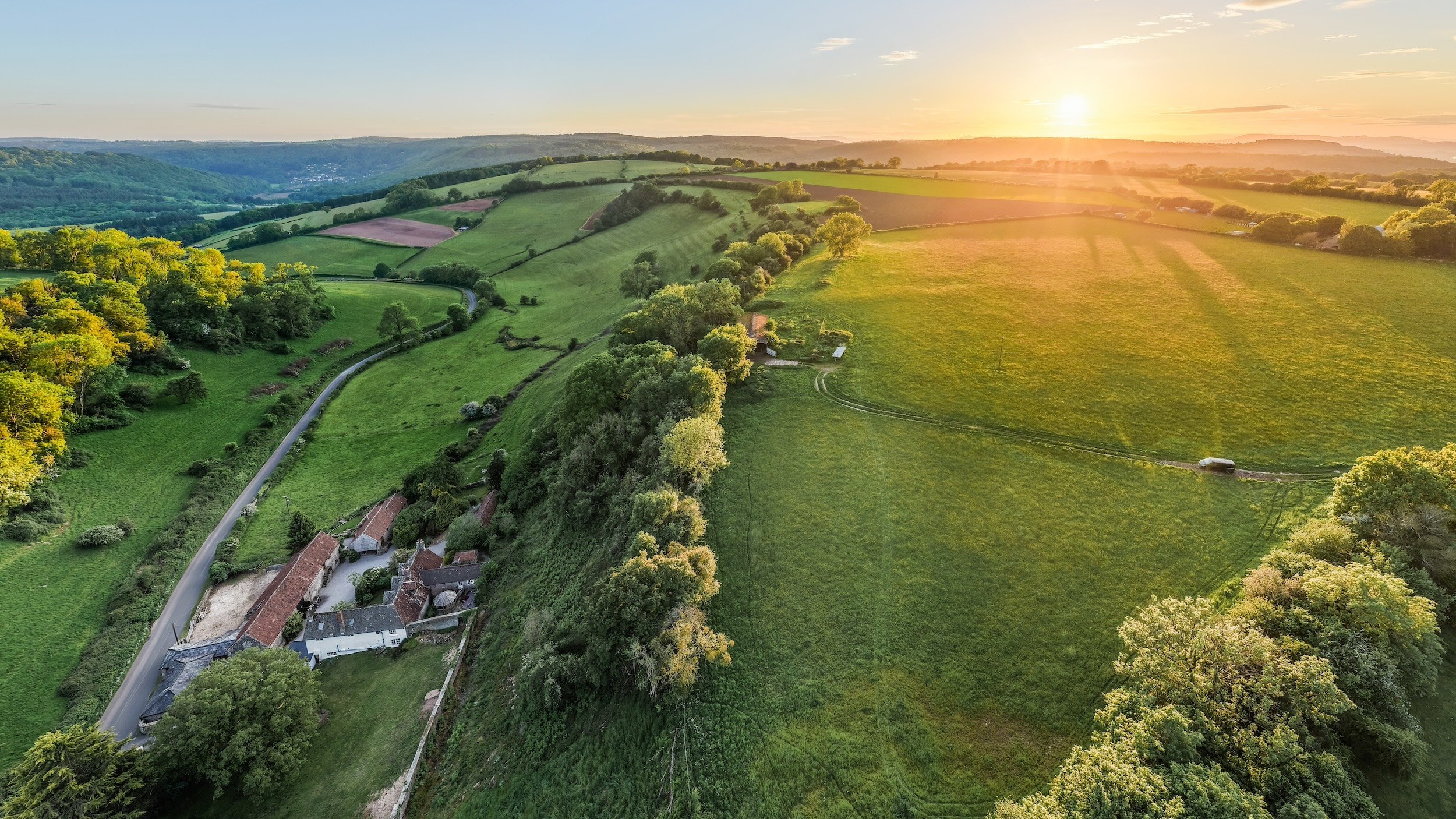 Aerial view of the From Stone To Sky film estate in the Forest of Dean, showing rolling countryside, woodland and production locations at golden hour.