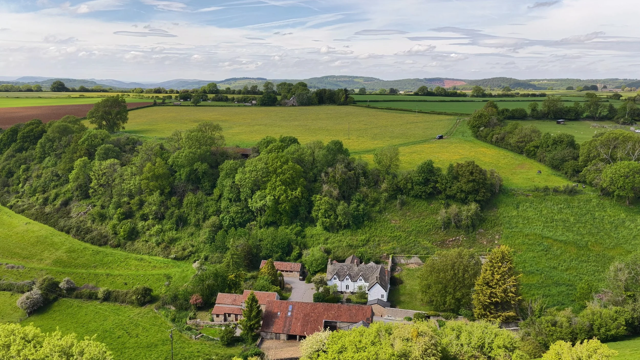 Aerial view of From Stone To Sky, with the historic farmstead surrounded by fields and woodland in the Wye Valley.