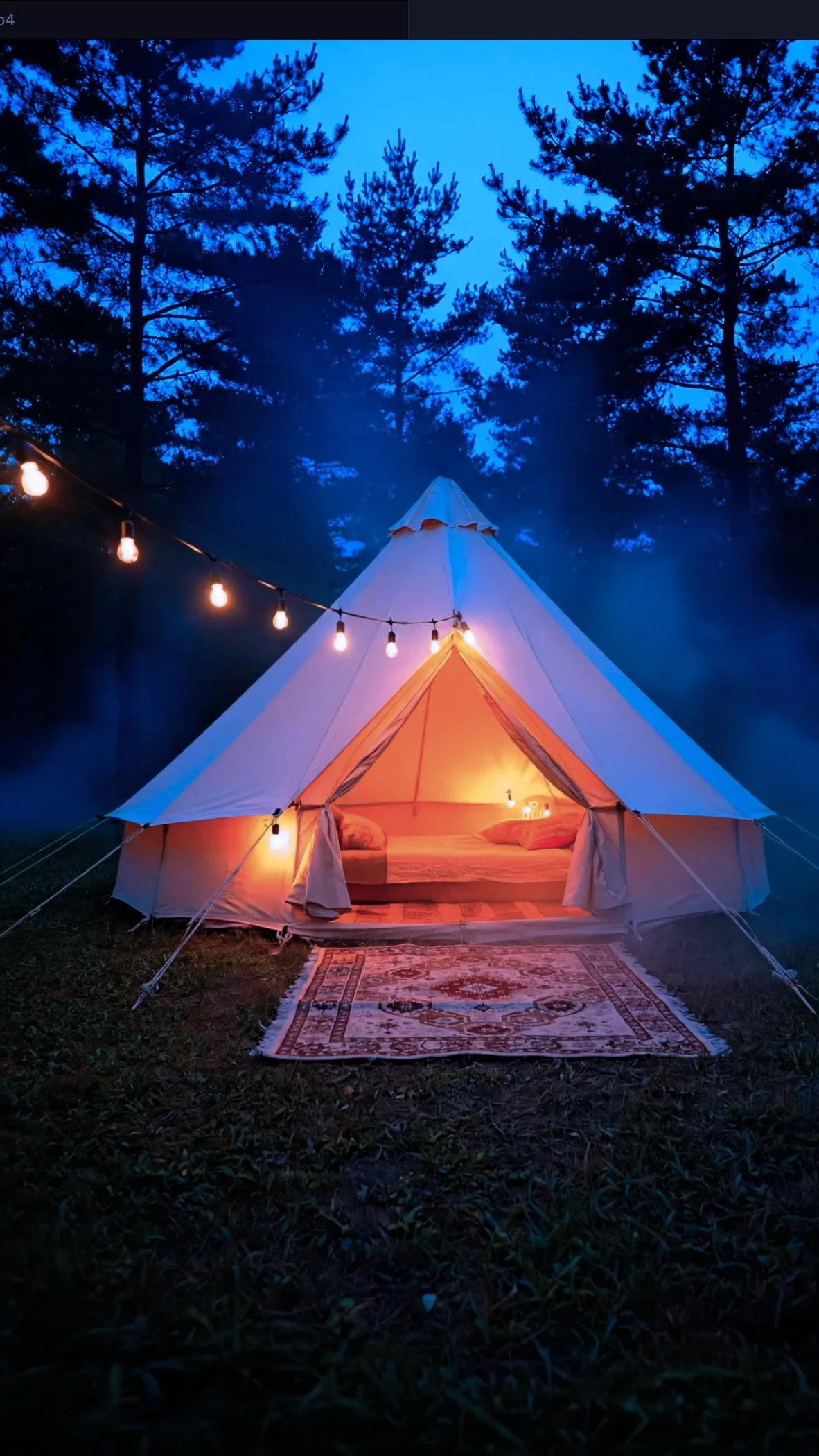 A cozy bell tent lit from within, set up outdoors in a wooded area at dusk, with string lights hanging above and a patterned rug on the ground leading to the entrance.