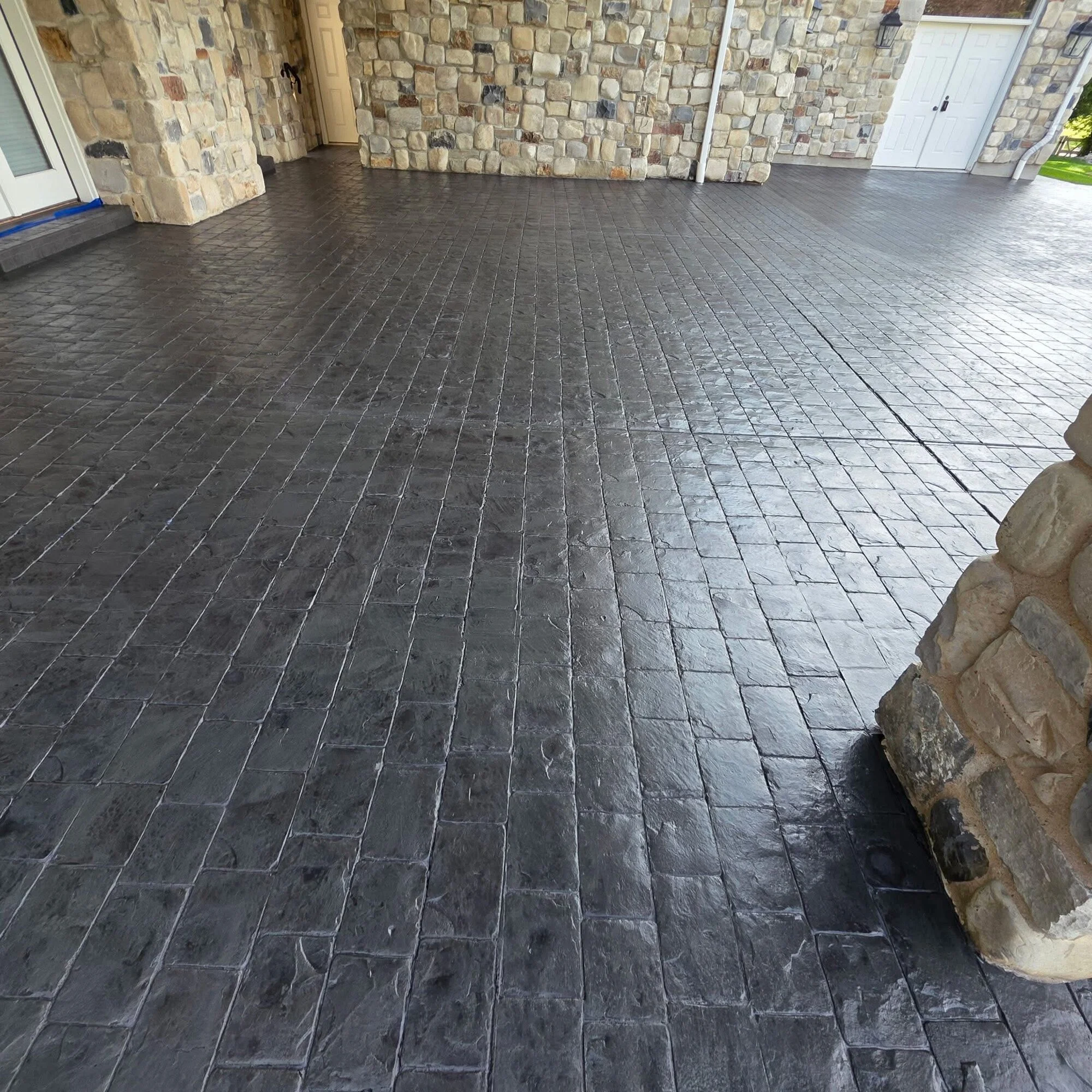 Stamped concrete patio in a charcoal ashlar slate pattern wrapping a stone-clad Utah home