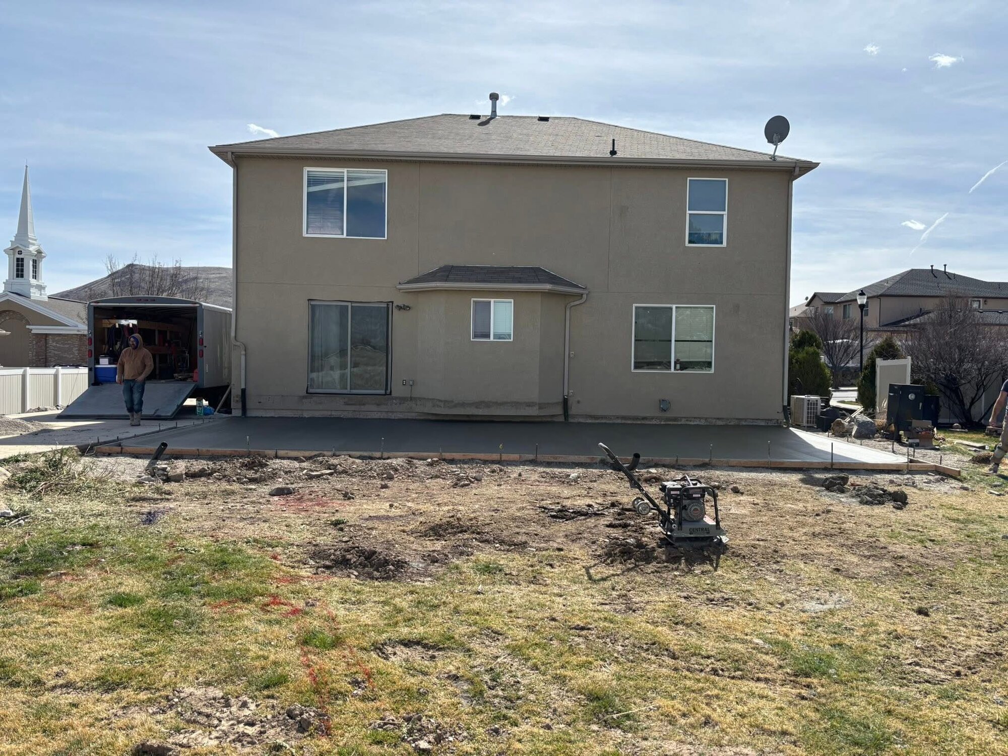 Wide backyard concrete patio slab poured across the rear of a two-story Utah home