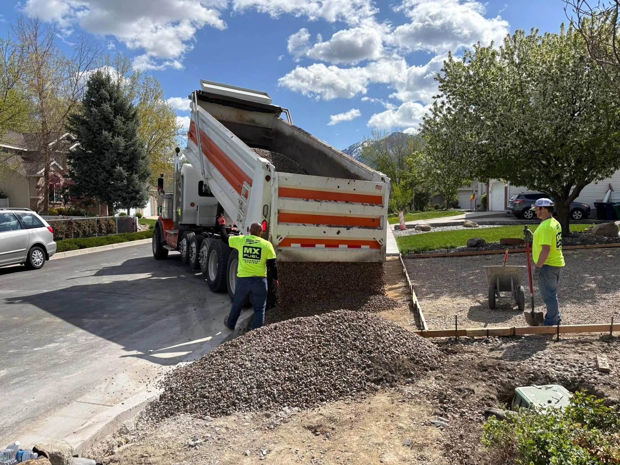 Dump truck delivering road base for driveway sub-grade preparation, with the Wasatch mountains behind