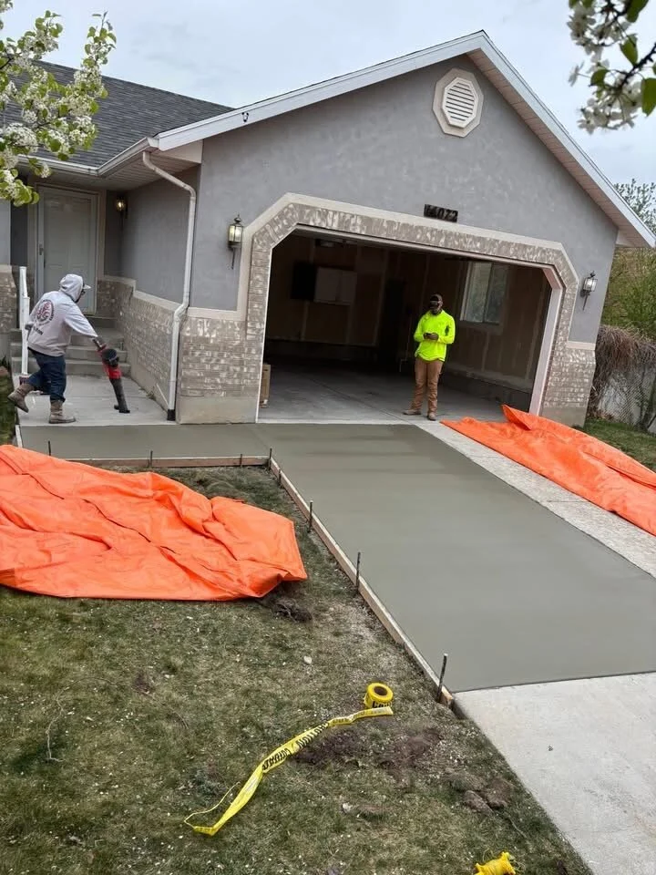 Freshly poured concrete driveway with curing blankets staged alongside during a residential replacement
