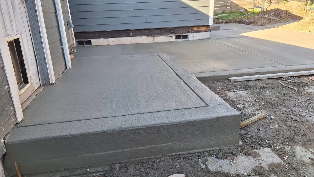 Newly poured concrete steps and sidewalk in front of a house under construction.