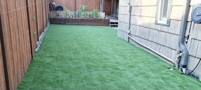 Backyard with artificial grass, wooden fence, and gray house siding