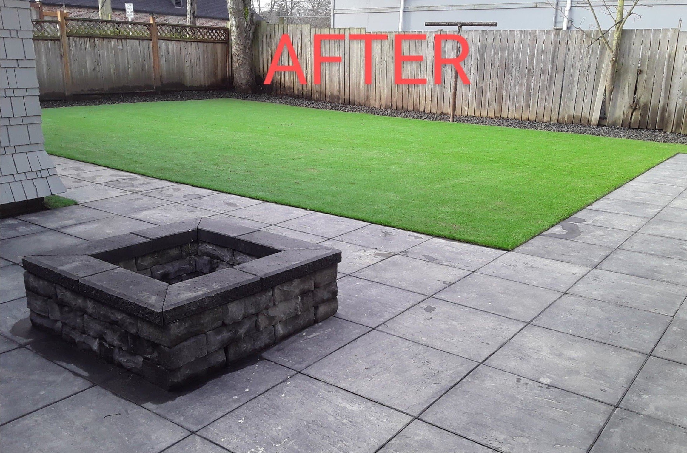A backyard patio with grey stone tiles, a stone fire pit in the foreground, a green artificial grass lawn behind it, and wooden fences around the perimeter, with the word 'AFTER' written in red across the image.