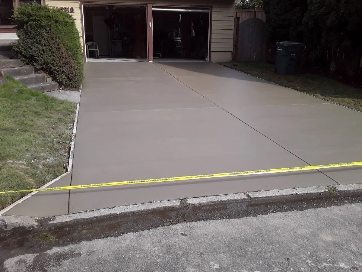 Freshly poured concrete driveway in front of a garage, with a caution tape across the edge.