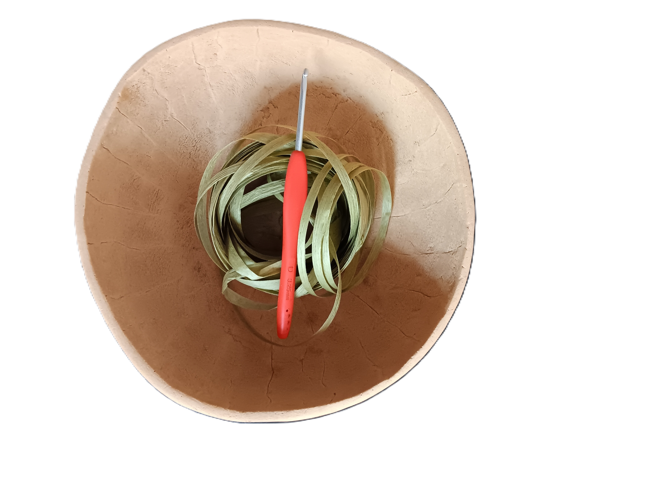 Green raffia yarn in a round, light brown gourd bowl. Crochet hook with orange handle is inserted into the yarn.