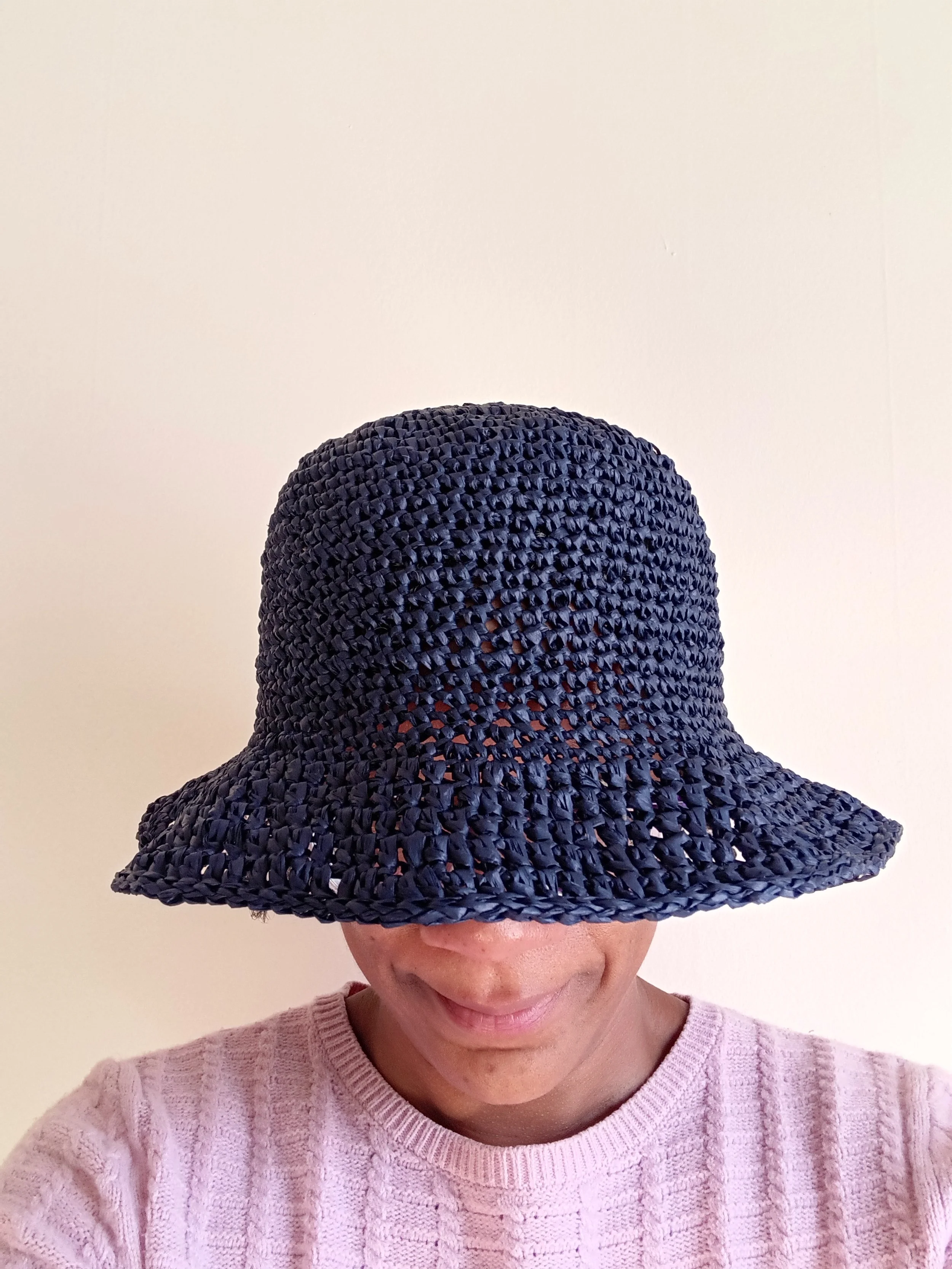 Person wearing a large, woven, navy blue sun hat, with only the mouth, chin, and part of a pink sweater visible.