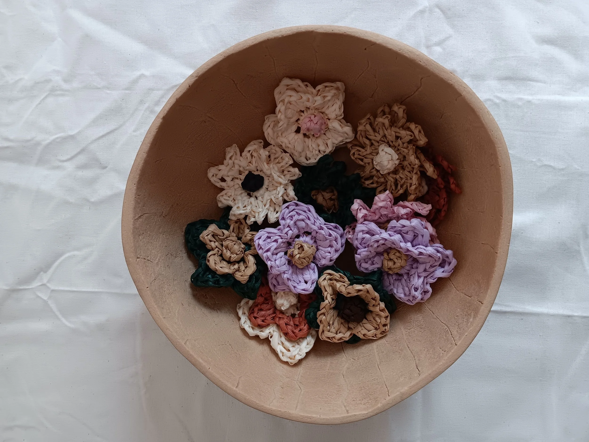 Decorative embroidery hooks resting inside a round wooden tray on a white tablecloth.