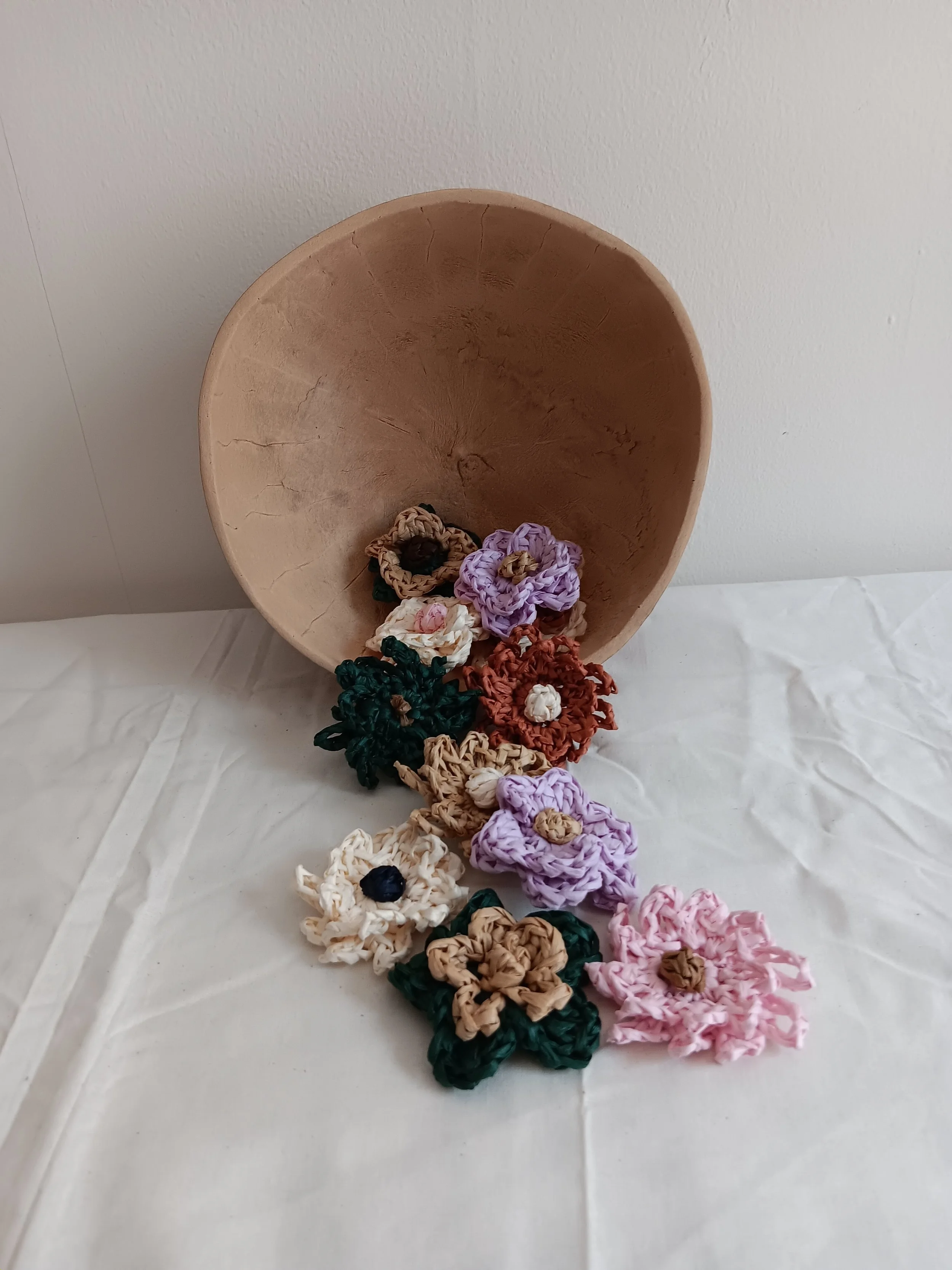 Gourd bowl tipped over on a white surface, with colorful crochet flowers spilling out of it.