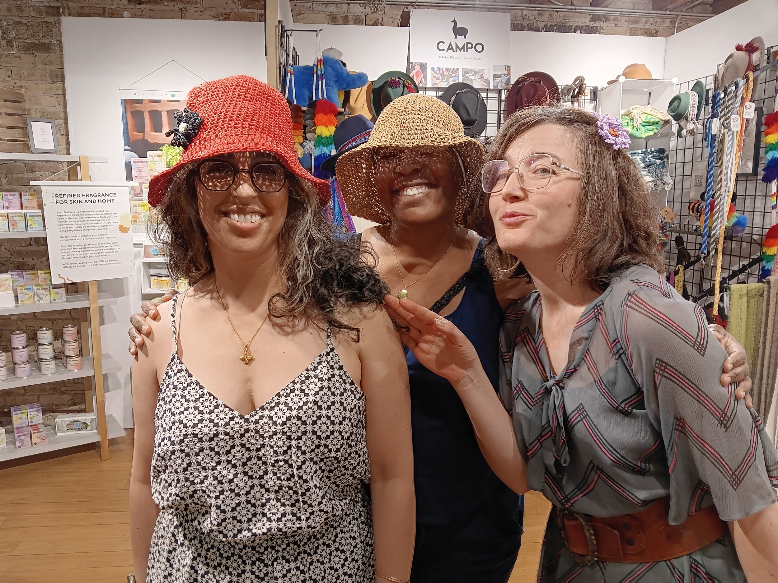 3 people smiling with 2 wearing hats and 1 wearing flower comb
