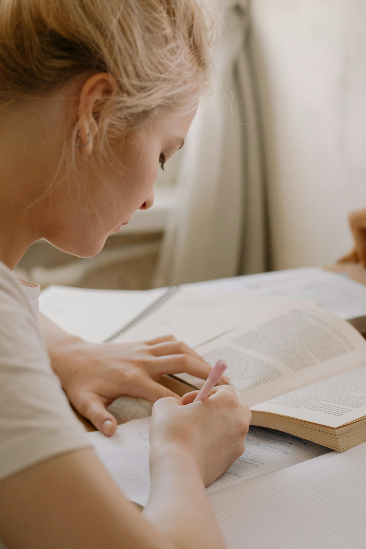 Eine junge Frau lernt oder arbeitet an einem Tisch, liest ein Buch und schreibt in ein Heft.