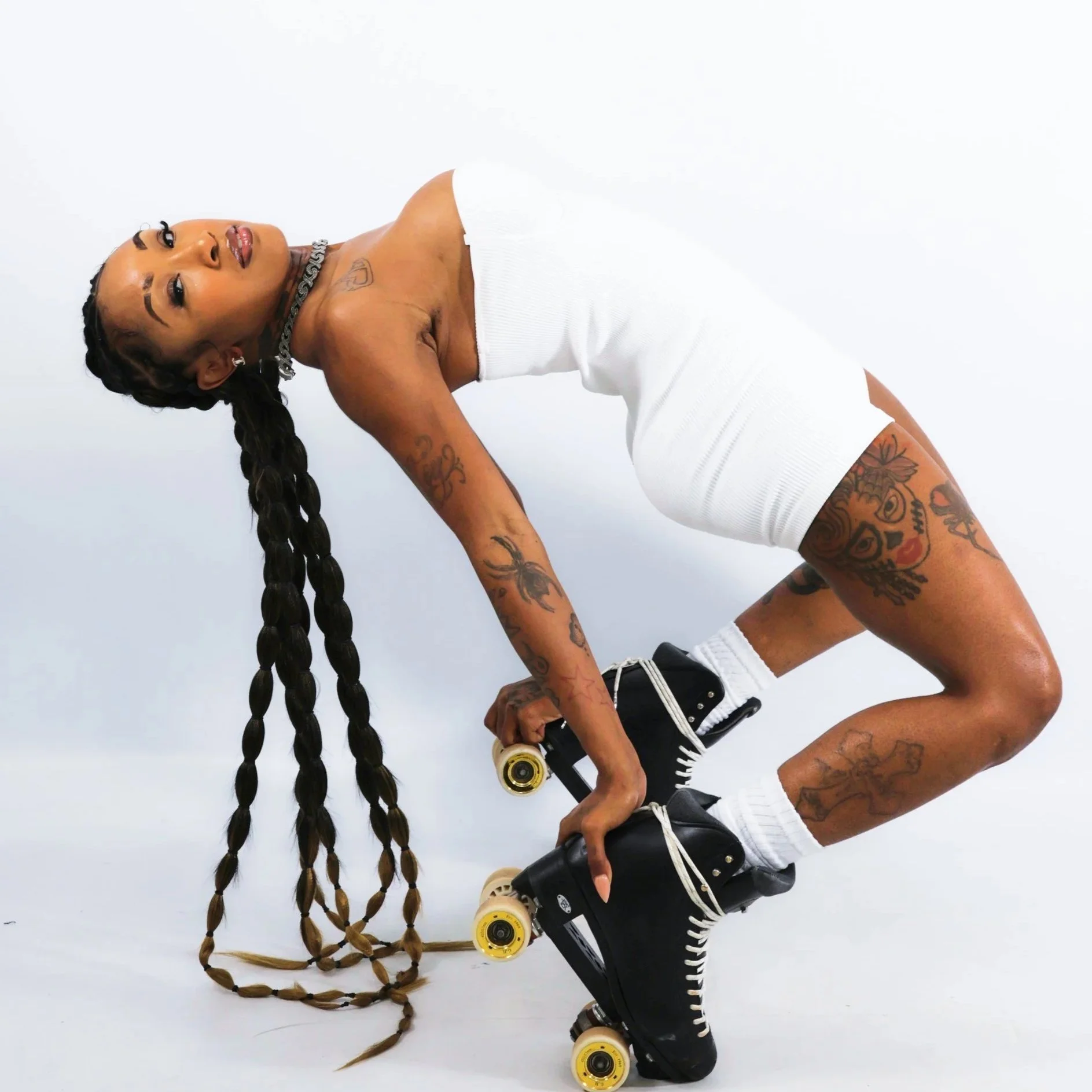 A woman with long braided hair, tattoos, and jewelry, dressed in a white outfit, wearing roller skates, and holding a bottle, posing against a white background.