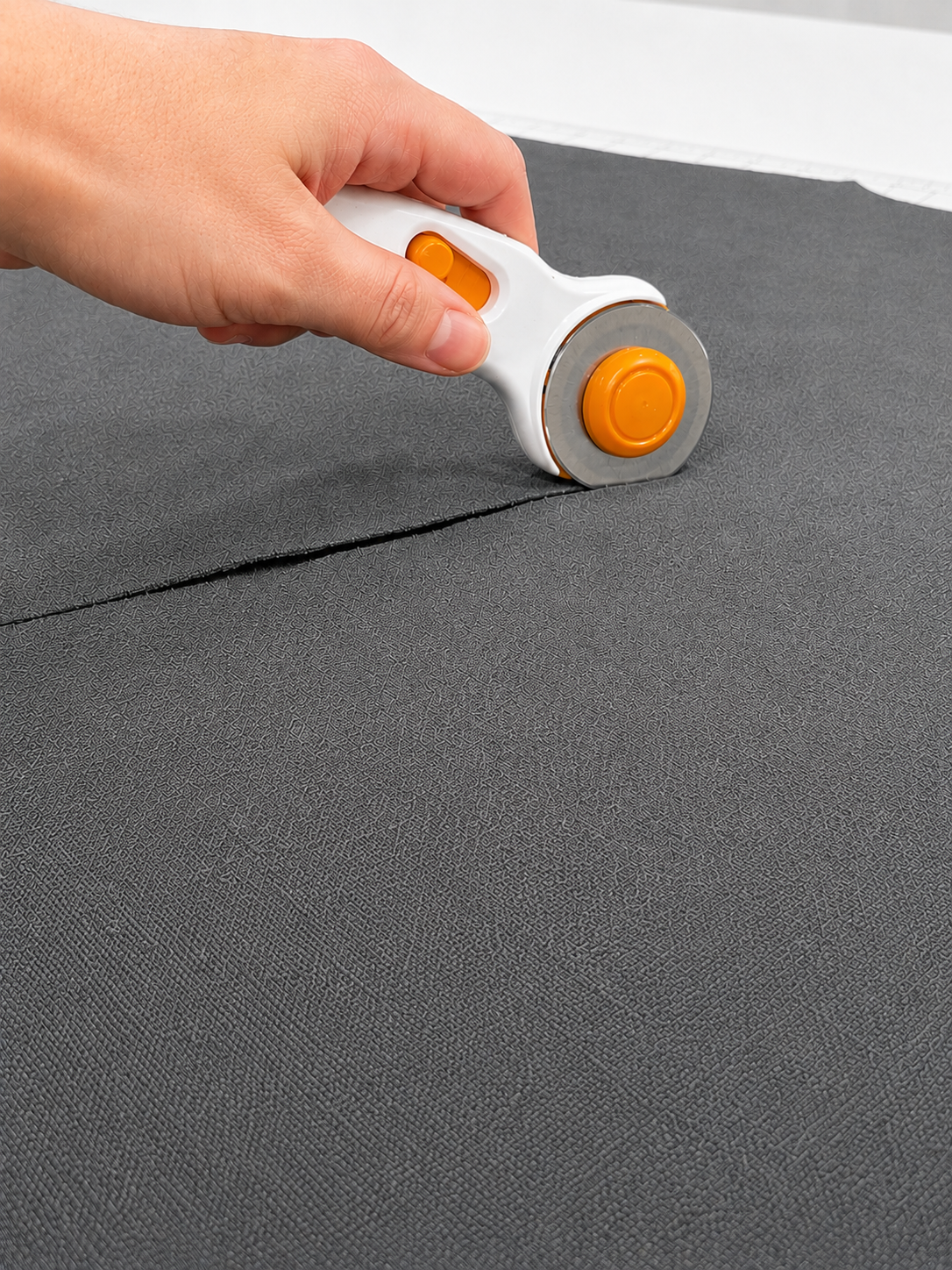 A hand holding a rotary cutter cutting through black fabric on a cutting mat.