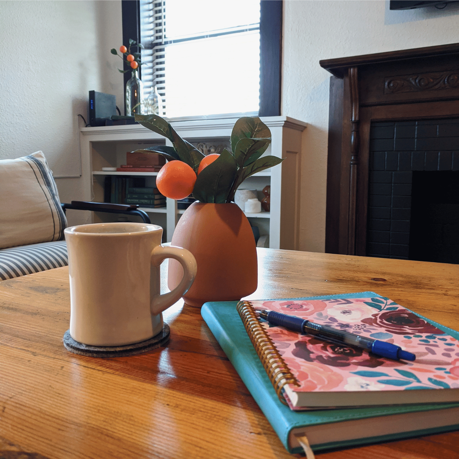 Coffee, journals, and a vase of oranges on a wooden table
