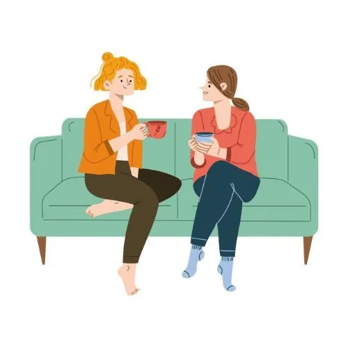 Two women sitting together on a couch, talking over cups of coffee