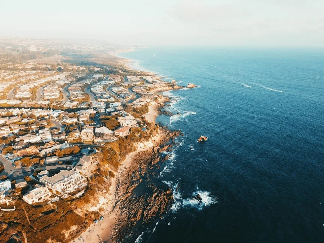 Aerial view of a coastal residential area with houses along the rocky cliffs and ocean.