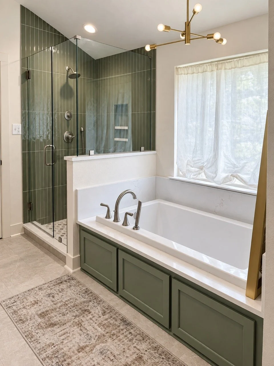 Green-accented primary bathroom with glass shower and soaking tub by Young Homes