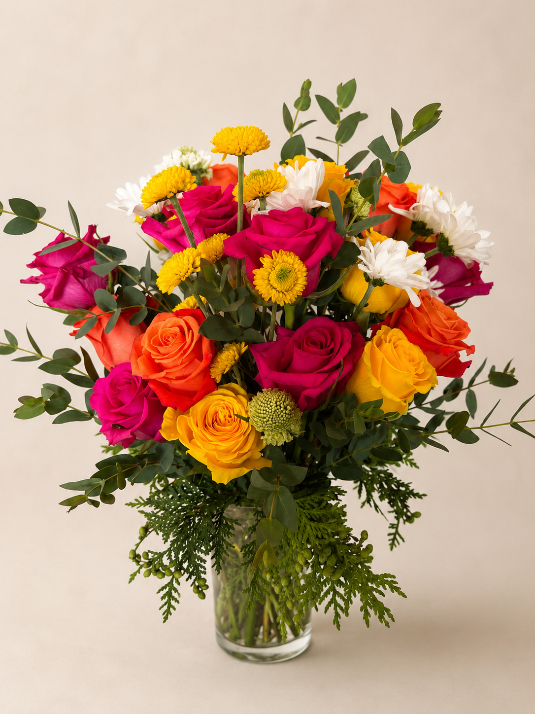 Colorful flower bouquet with pink, yellow, orange roses, white daisies, and greenery in a glass vase