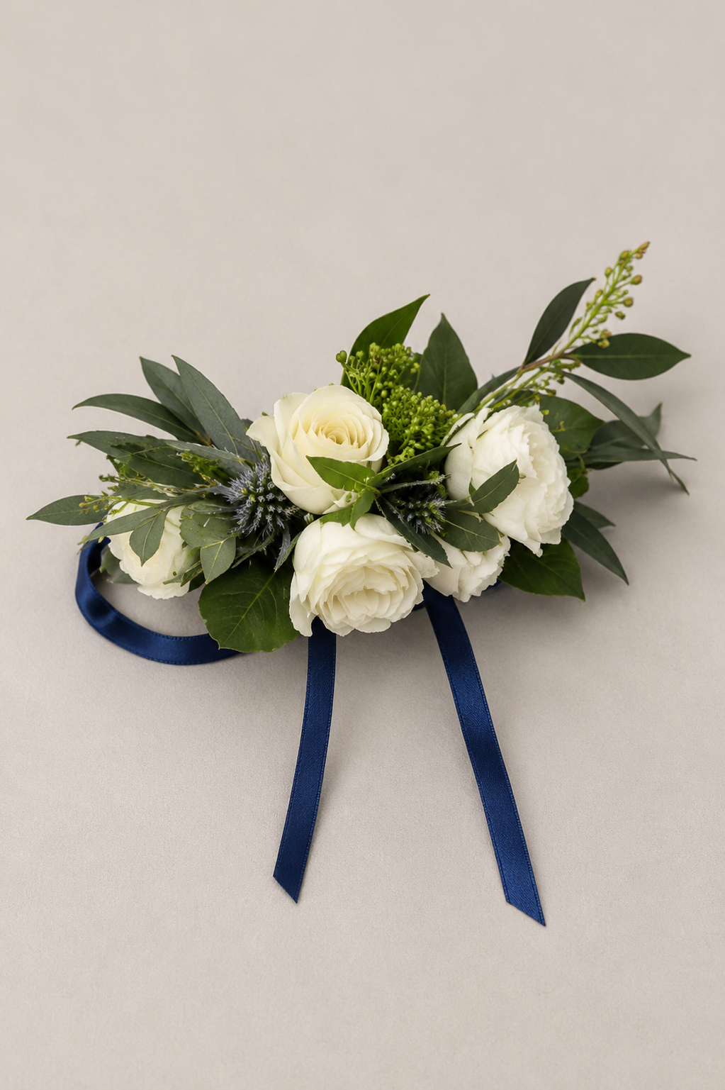A boutonniere with white flowers, greenery, and a blue ribbon