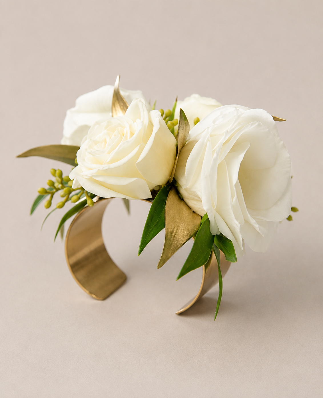 A floral arrangement with white roses, green leaves, and small yellow buds in a gold-colored crescent-shaped holder.