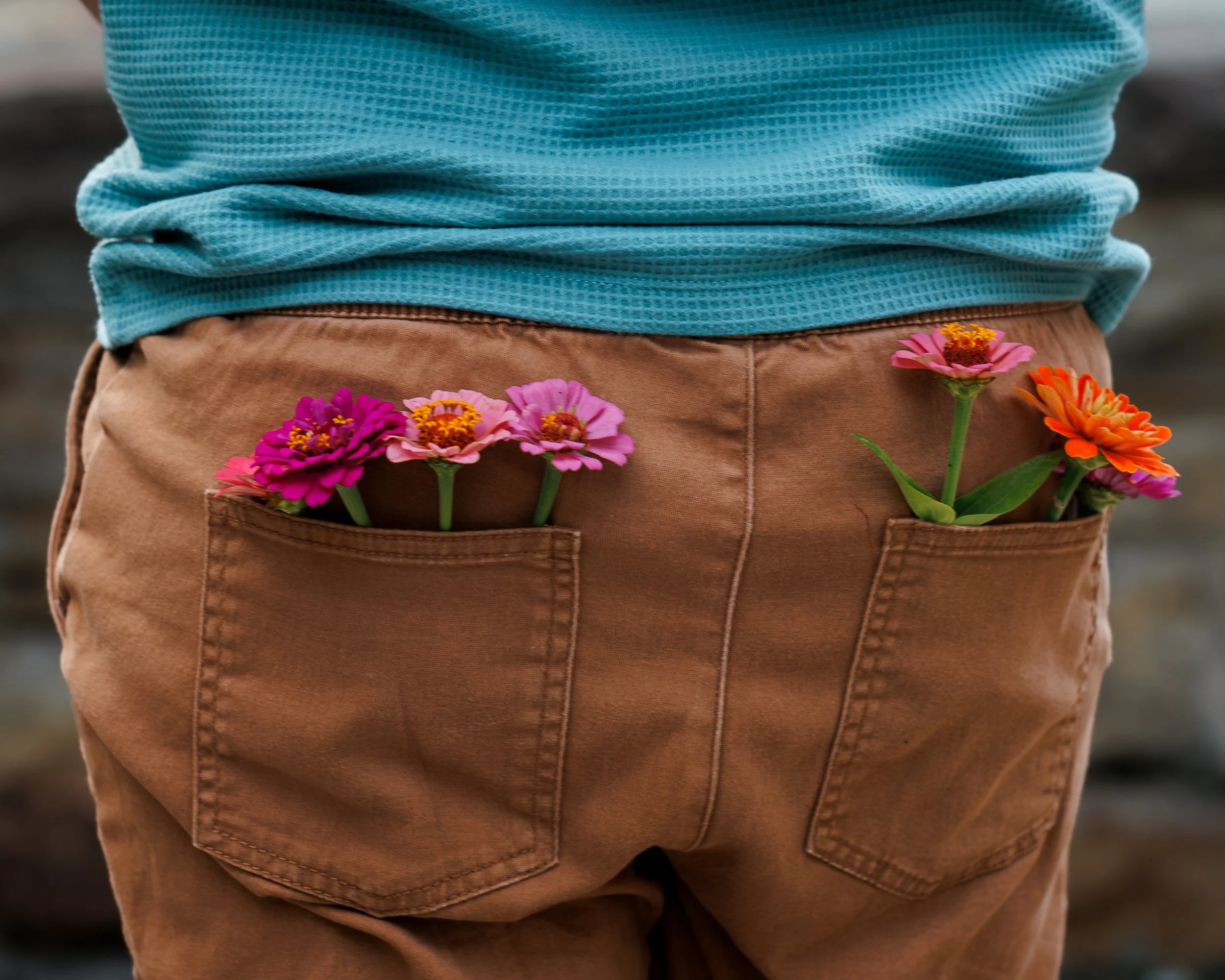 A person wearing a blue textured shirt and tan pants with a pocket that has colorful flowers in it.