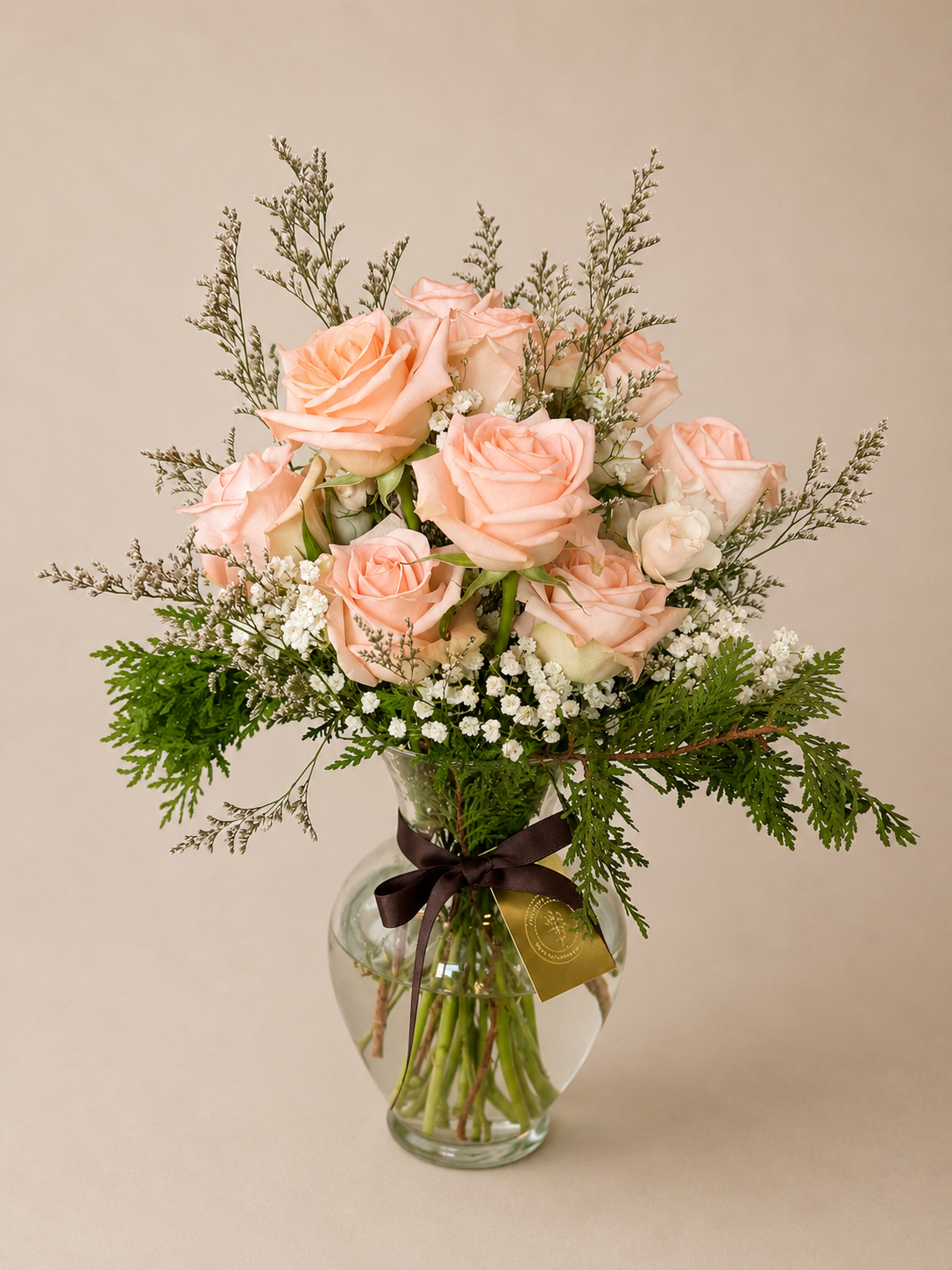 A vase with a bouquet of light pink and white roses, baby's breath, and greenery, tied with a black ribbon.
