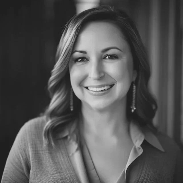 Black and white portrait of a smiling woman with wavy shoulder-length hair, wearing earrings and a collared shirt.