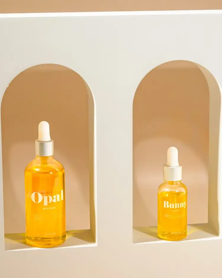 Two amber-colored dropper bottles with white droppers inside a light-colored display shelf, labeled 'Opal' and 'Bunny'.