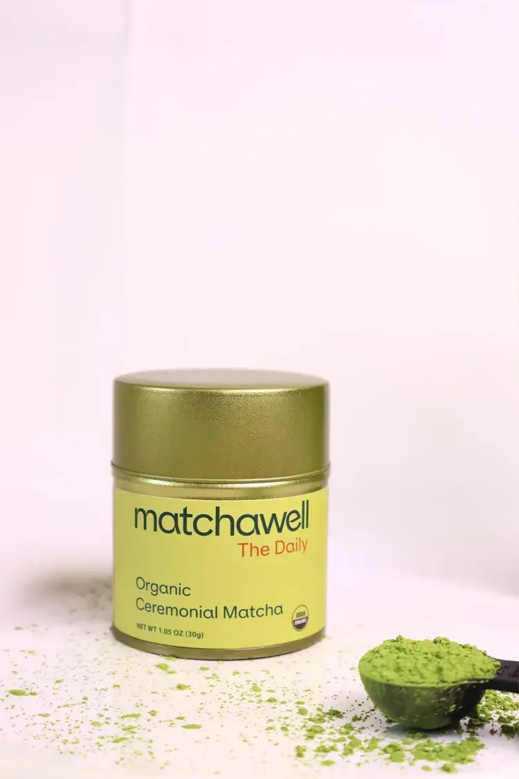 Container of MatchaWell The Daily Organic Ceremonial Matcha with a scoop of green matcha powder beside it.