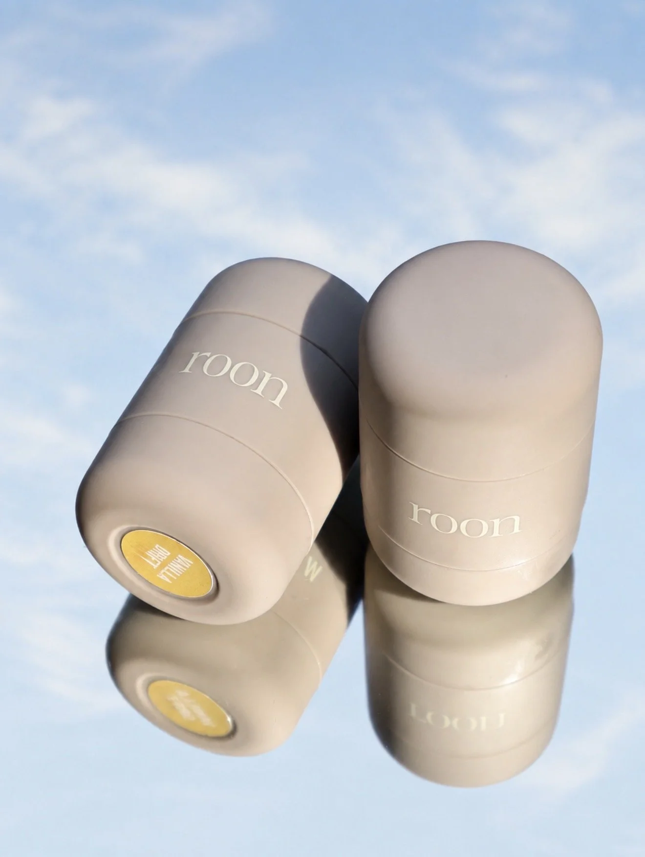 Multiple beige large candles with the word 'roon' on them, placed outdoors against a blue sky with some clouds.