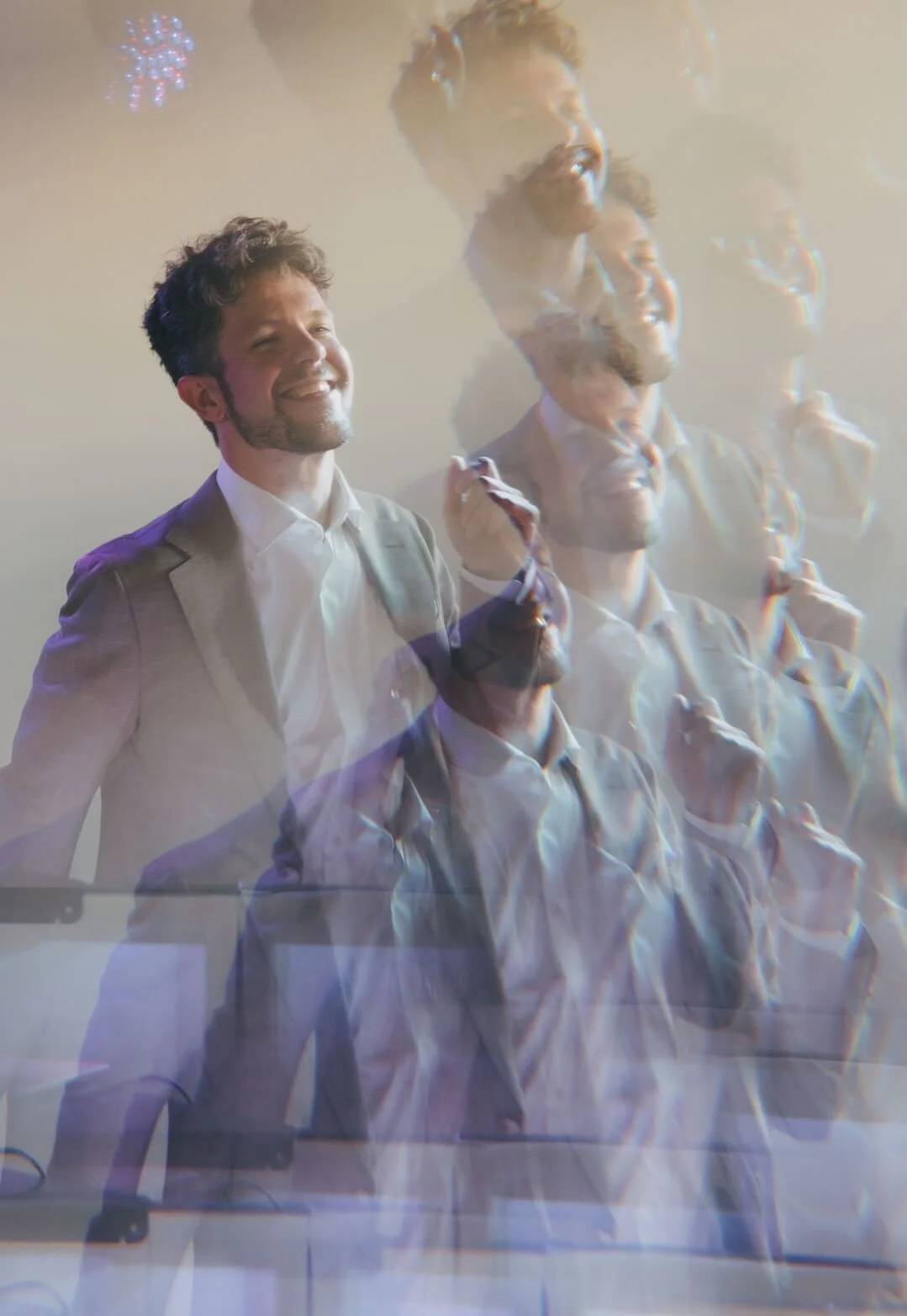 Multiple overlapping images of a smiling man in a suit holding a microphone, creating a layered effect.