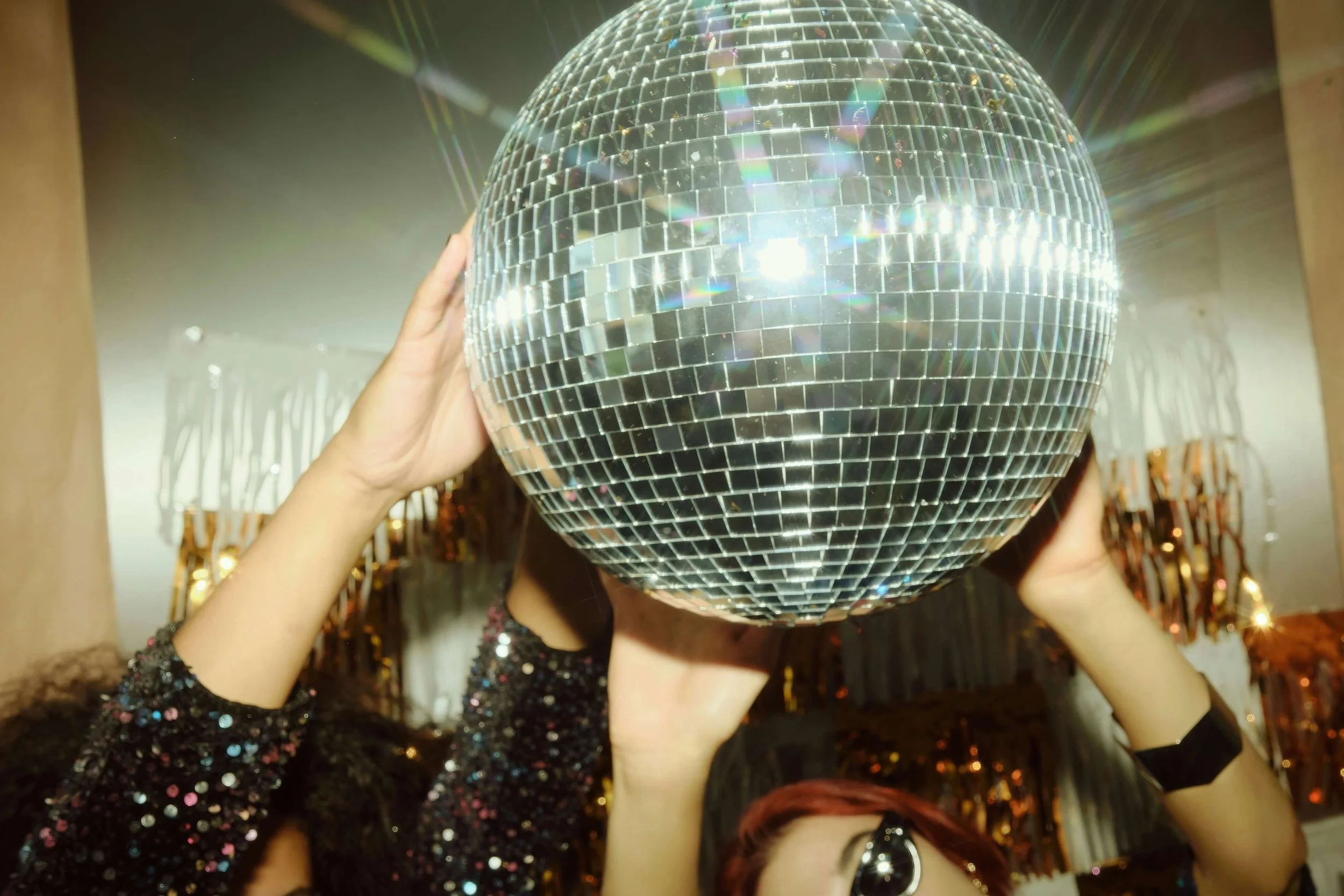 Person holding a large disco ball up to their face at a party or celebration.
