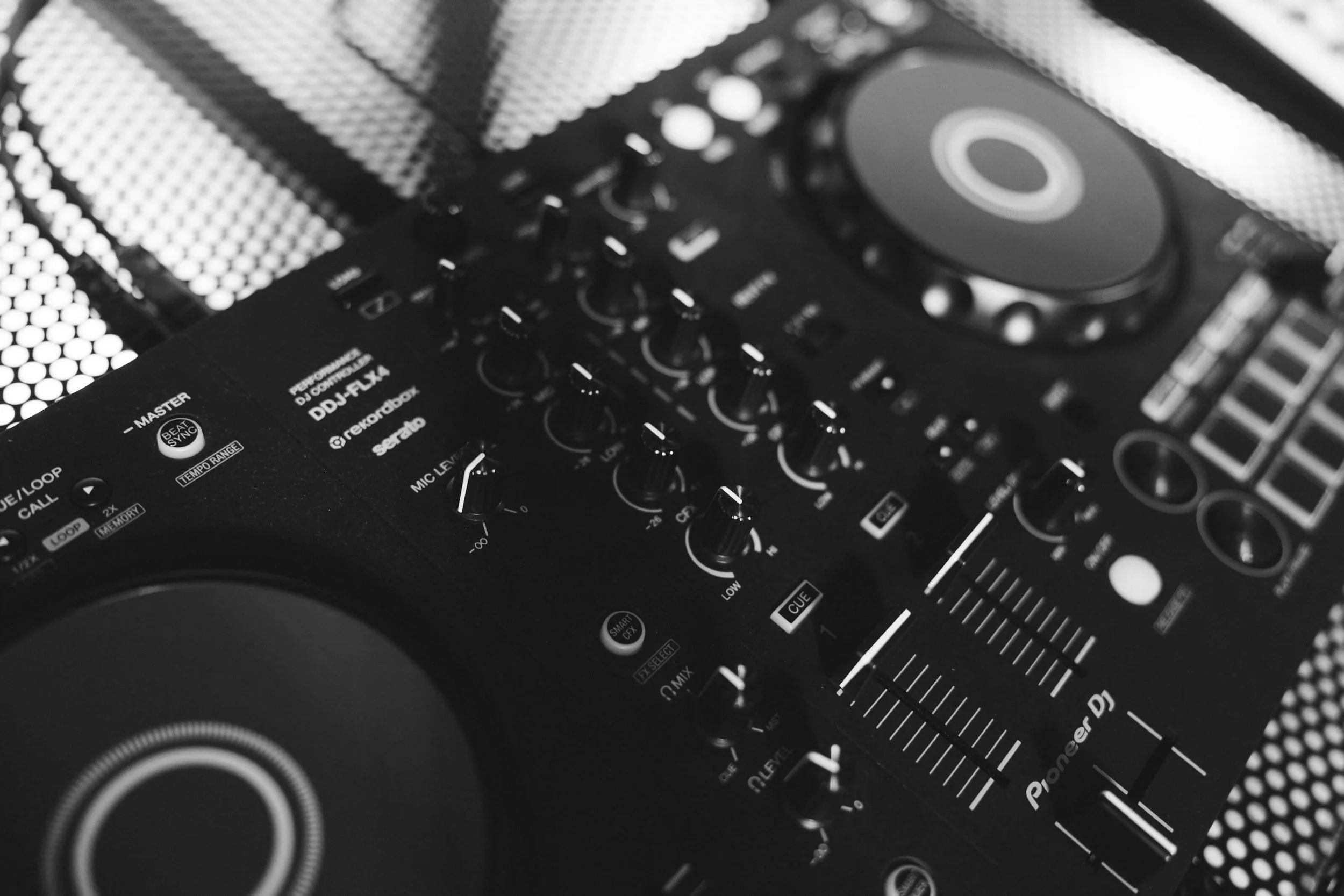 Close-up of a DJ mixer and turntable with various knobs, buttons, and controls in black and white.