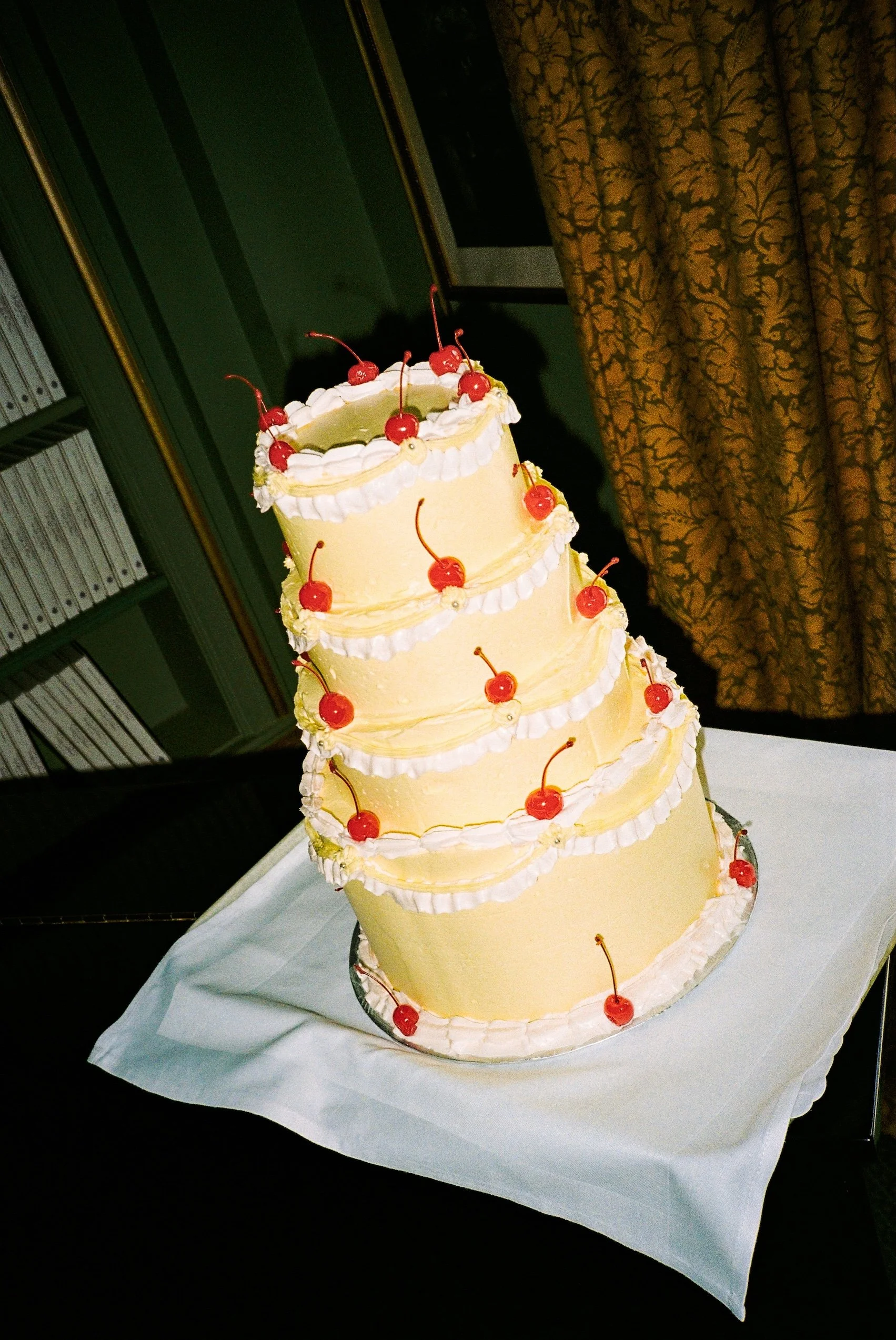 A multi-tiered cake decorated with cherries and white frosting, set on a table with a white tablecloth.