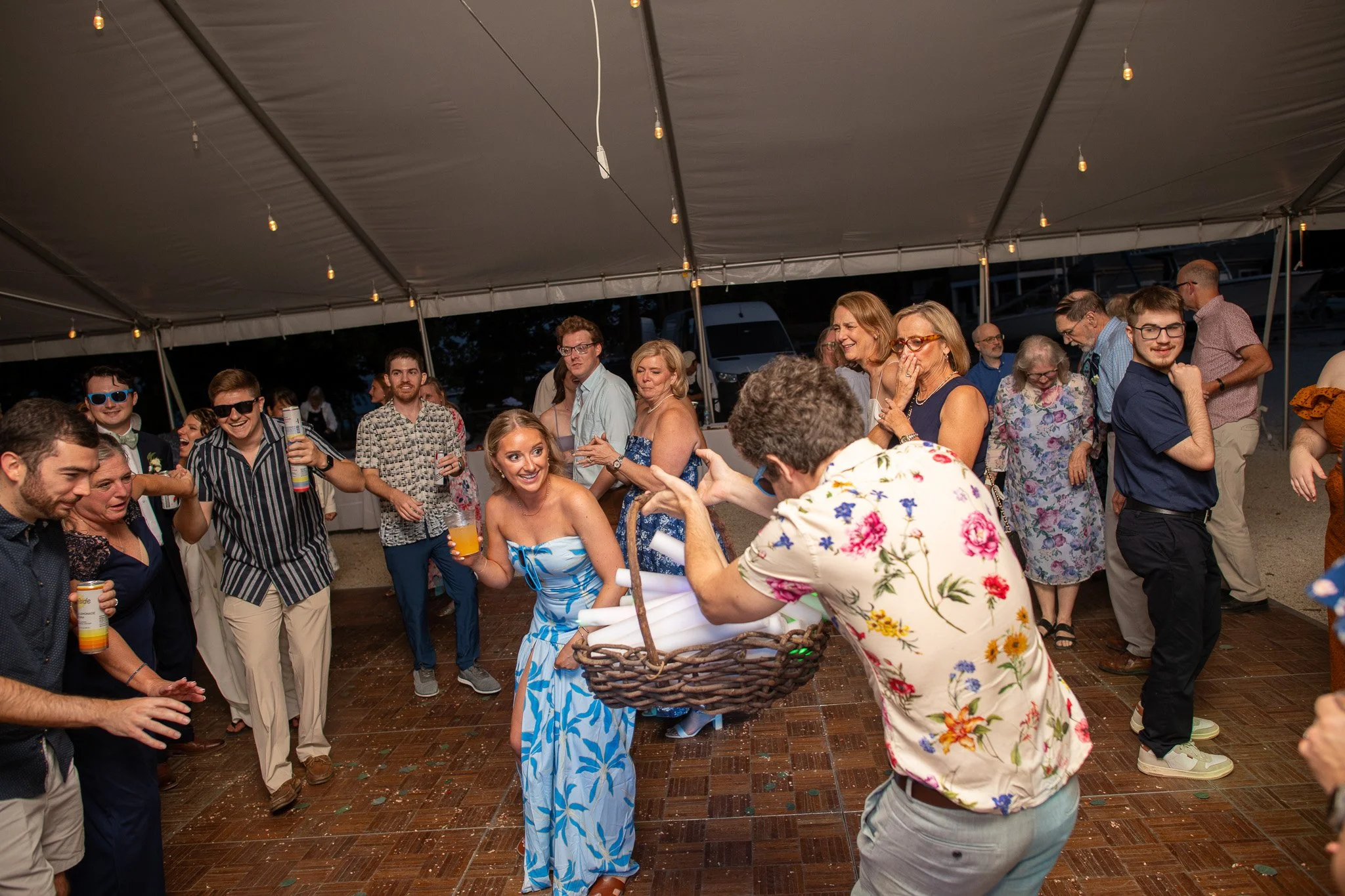 Group of people dancing and socializing under a large tent at an outdoor event, with some holding drinks and smiling.