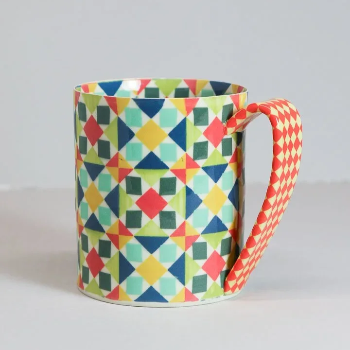 Colorful patterned ceramic mug with a geometric design and a contrasting diamond pattern on the handle by Lydia Johnson