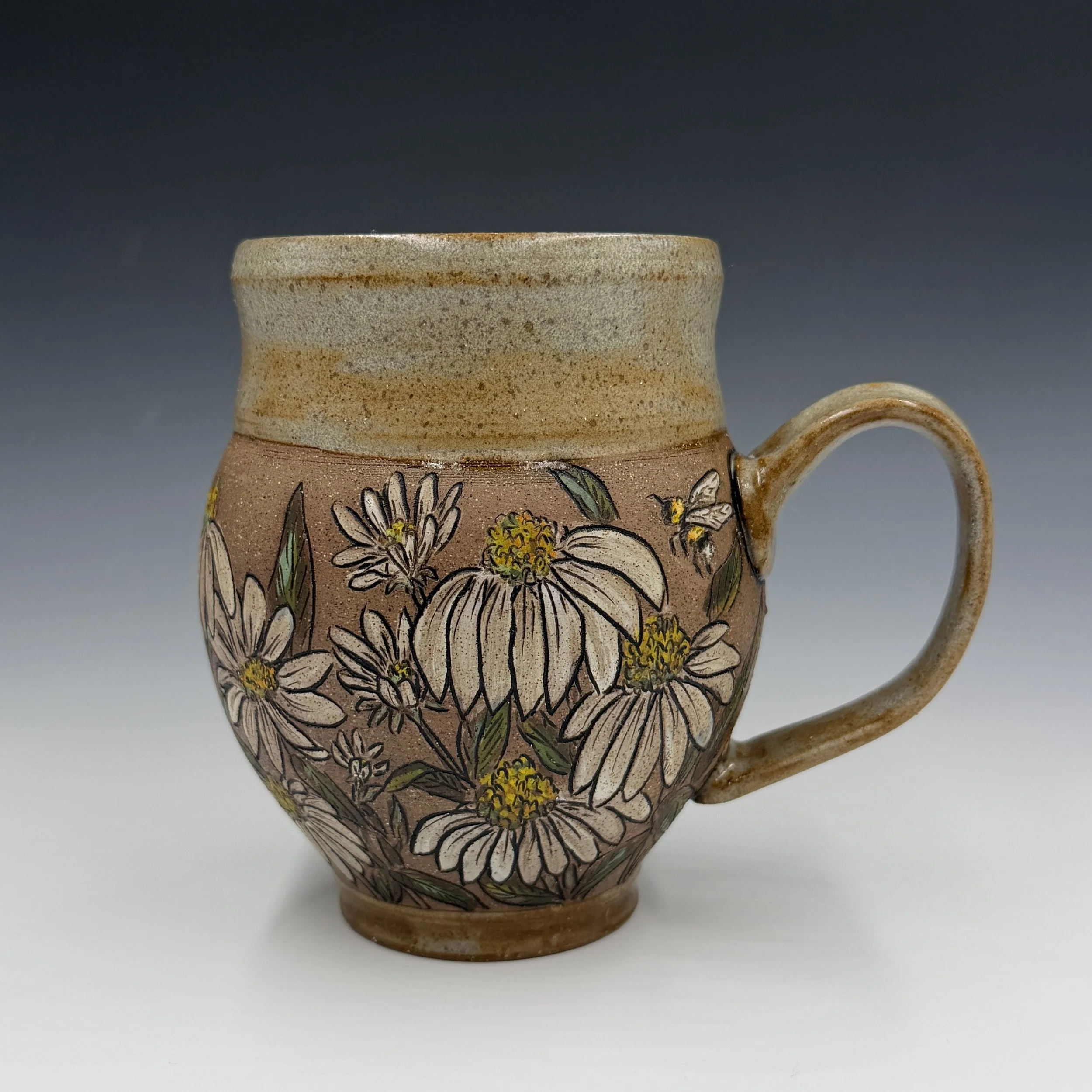 Close-up of a handcrafted ceramic mug with floral and botanical painted design, featuring daisies and yellow flowers, against a plain gray background. - Stephanie Haines