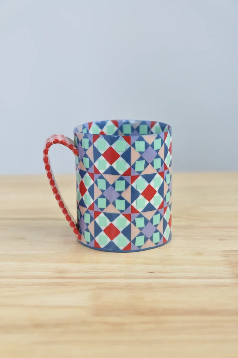 Colorful mug with a geometric pattern resting on a wooden surface by Lydia Johnson