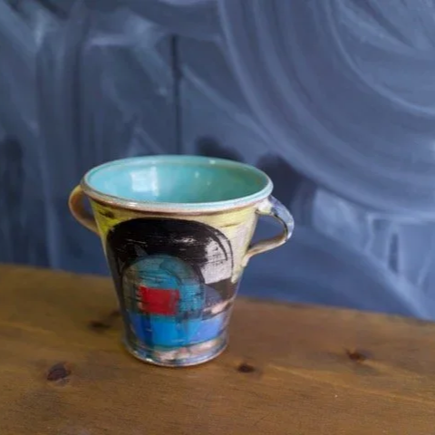 Decorative ceramic mug with abstract colorful design on a wooden surface by Pedro Centeno