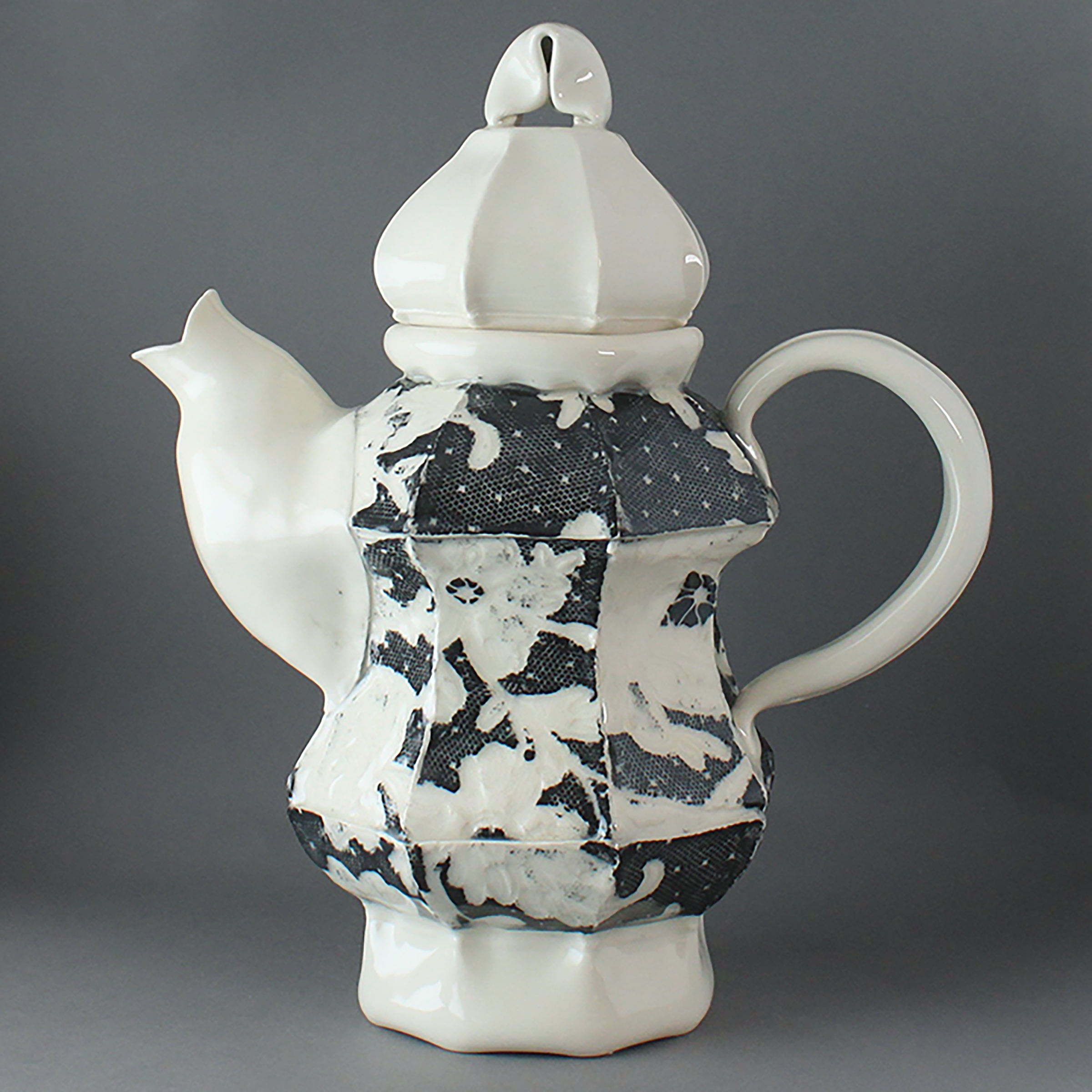 A white ceramic teapot with a black and white patterned fabric draped underneath and a plain gray background. - Elyse Cote